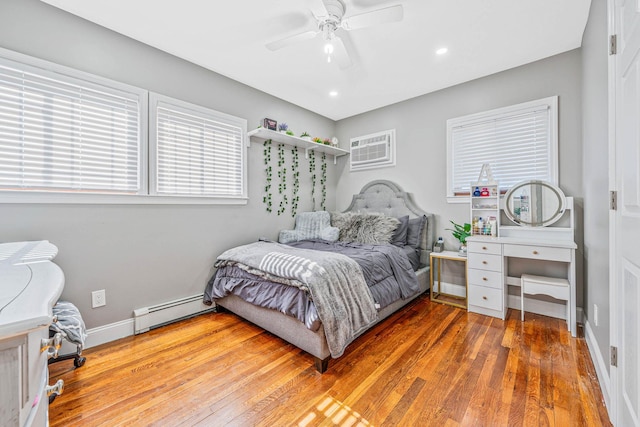 bedroom with wood-type flooring, a baseboard heating unit, ceiling fan, a wall mounted air conditioner, and baseboards