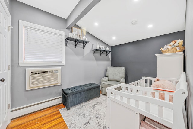 bedroom with a baseboard radiator, baseboards, wood finished floors, and a wall mounted air conditioner