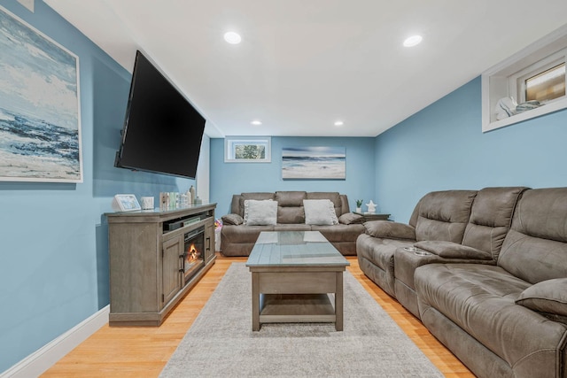 living area featuring light wood-style floors, a warm lit fireplace, baseboards, and recessed lighting