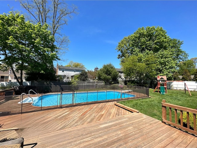 view of swimming pool with a deck, playground community, fence, a lawn, and a fenced in pool