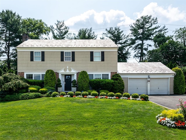 colonial house with driveway, a chimney, an attached garage, a front yard, and brick siding