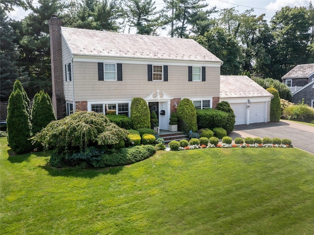 colonial home with driveway, a chimney, an attached garage, a front yard, and brick siding