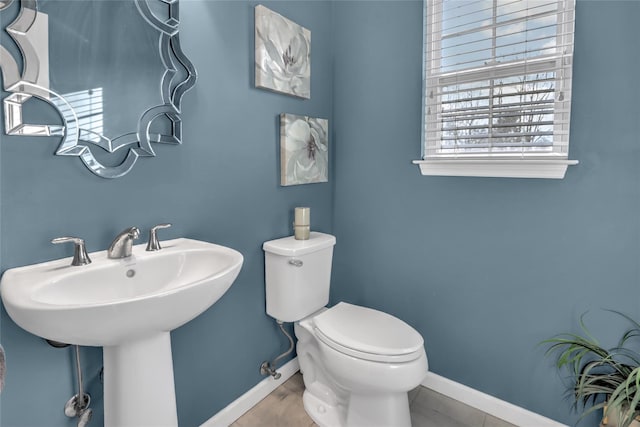 half bath featuring toilet, baseboards, and a sink