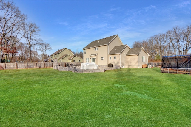 back of property with a trampoline, a fenced backyard, a yard, and exterior kitchen