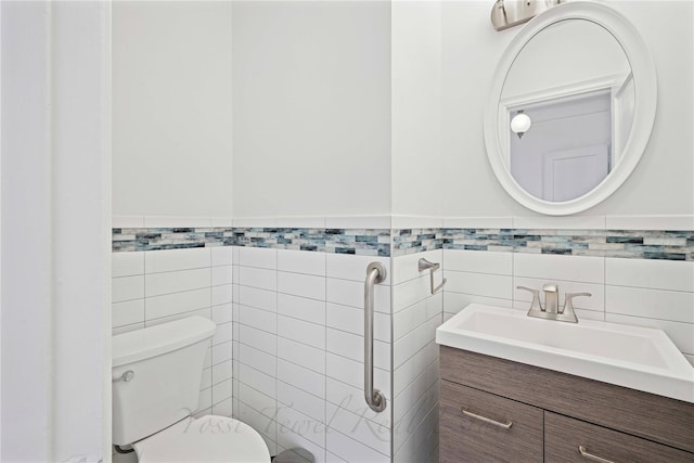 half bath featuring wainscoting, vanity, toilet, and tile walls