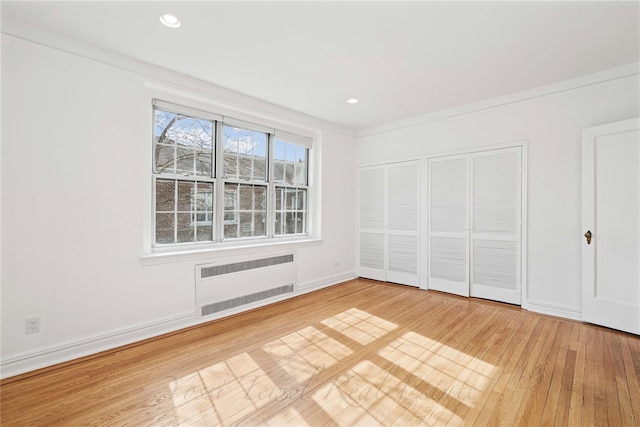 unfurnished bedroom featuring two closets, recessed lighting, radiator heating unit, light wood-type flooring, and baseboards