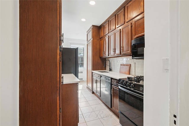 kitchen featuring tasteful backsplash, light countertops, black appliances, a sink, and light tile patterned flooring