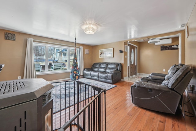 living room featuring light wood-style floors, visible vents, baseboards, and a wall mounted AC