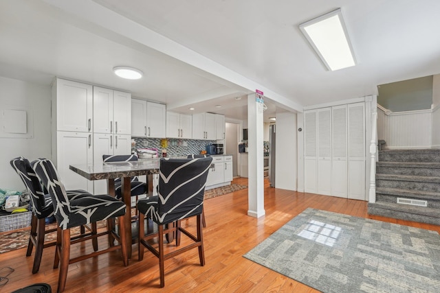 dining space featuring light wood-type flooring, visible vents, and stairway