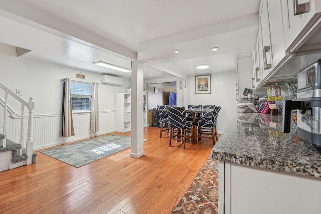 kitchen with dark stone counters, a wall mounted air conditioner, white cabinets, and light wood-style floors