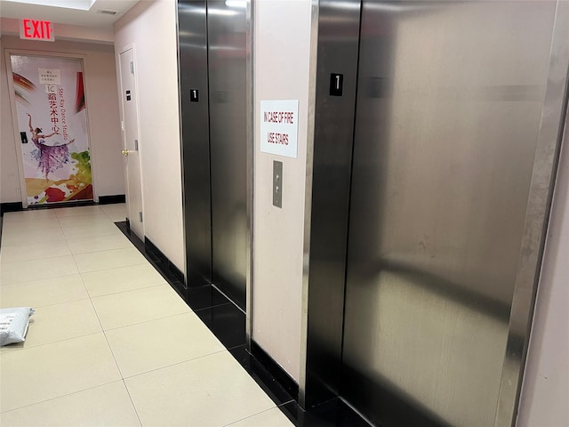 corridor featuring elevator, baseboards, and dark tile patterned flooring