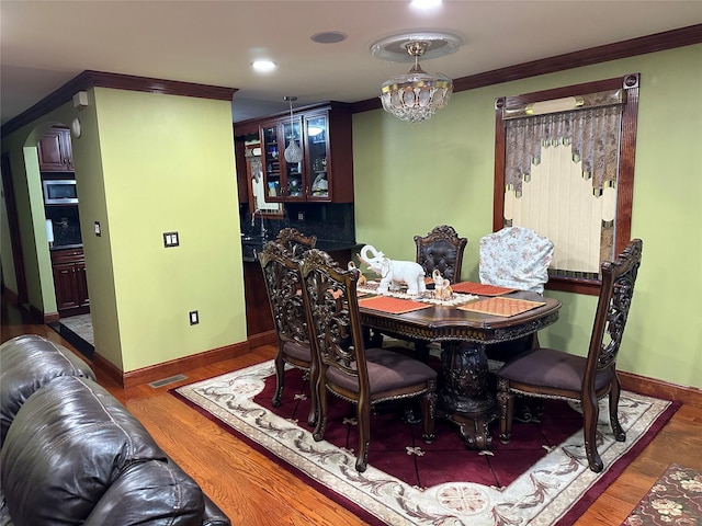 dining room featuring arched walkways, visible vents, crown molding, and wood finished floors