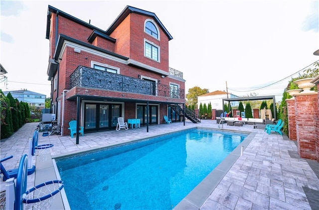 rear view of property featuring a fenced in pool, a balcony, stairs, a patio area, and brick siding