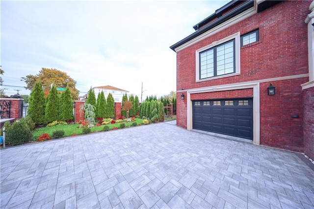 view of side of property featuring brick siding, decorative driveway, and an attached garage