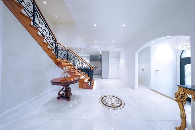 tiled entrance foyer featuring arched walkways, crown molding, recessed lighting, stairway, and baseboards