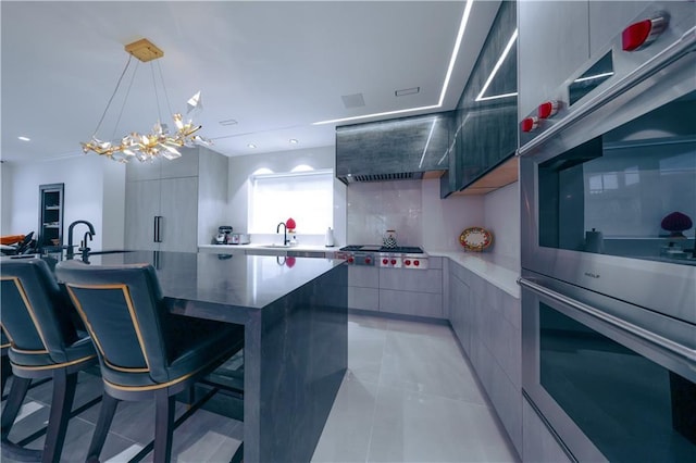 kitchen with wall chimney exhaust hood, modern cabinets, a kitchen breakfast bar, stainless steel appliances, and a sink