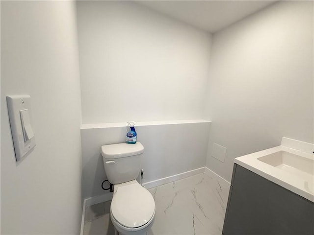 half bathroom with toilet, marble finish floor, baseboards, and vanity