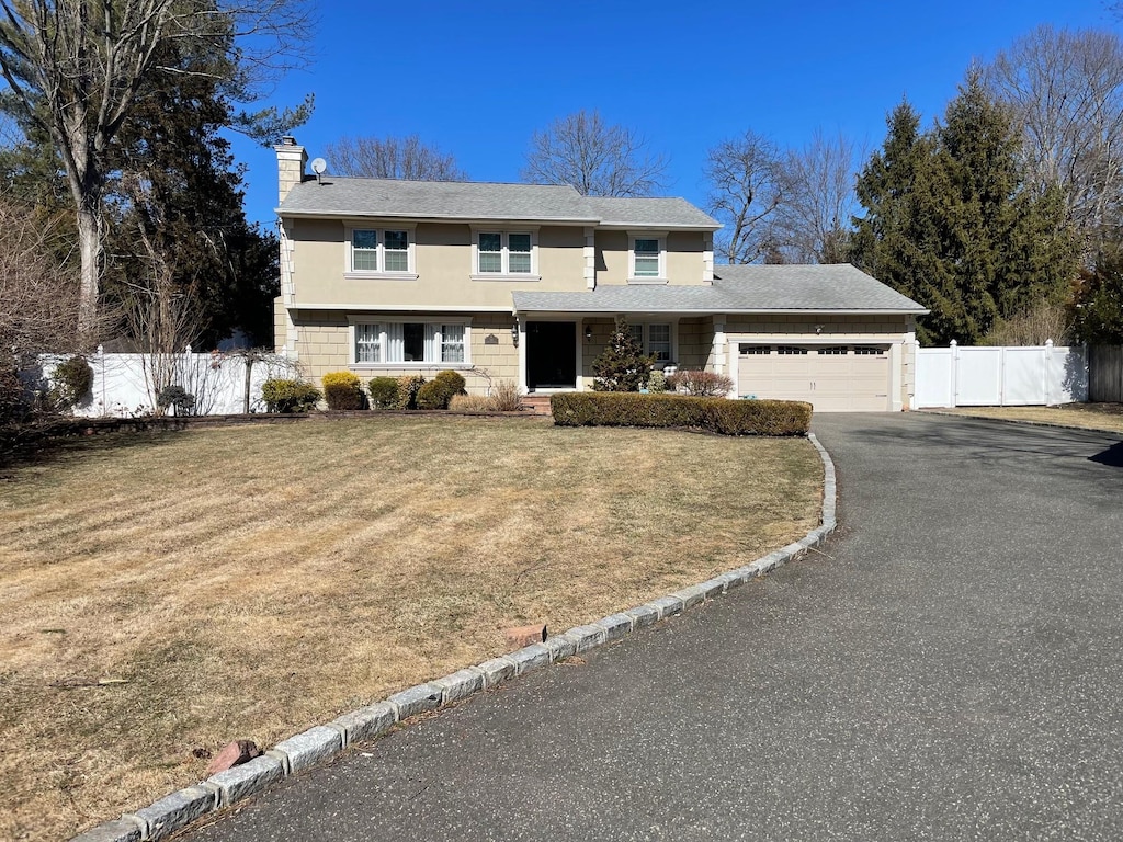 traditional-style home with a garage, a chimney, aphalt driveway, fence, and a front yard