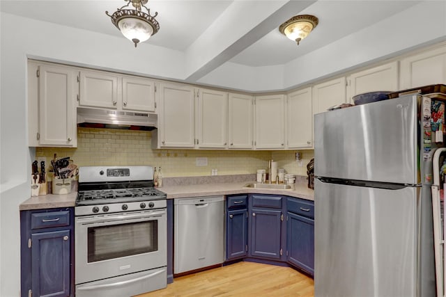 kitchen featuring blue cabinetry, stainless steel appliances, light countertops, under cabinet range hood, and a sink