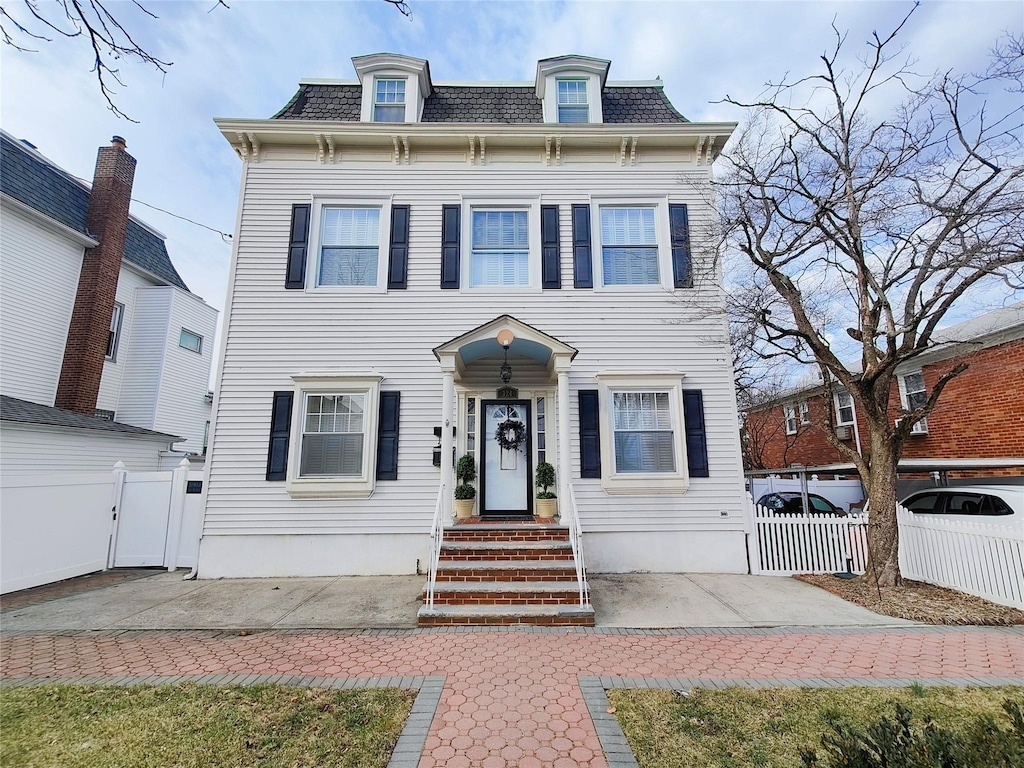 victorian home with a gate, fence, and mansard roof