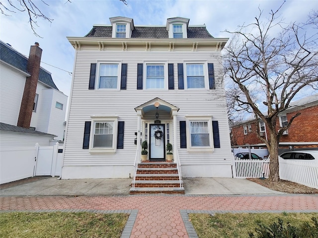 victorian home with a gate, fence, and mansard roof