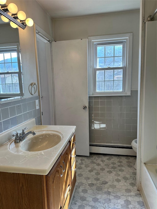 bathroom with toilet, a baseboard radiator, vanity, and tile walls