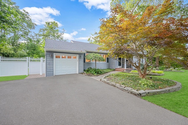 ranch-style home with a garage, driveway, roof with shingles, fence, and a front yard