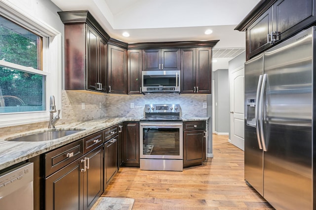 kitchen with tasteful backsplash, light stone counters, stainless steel appliances, and a sink