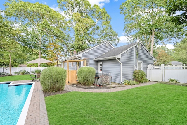 back of house featuring a fenced backyard, a fenced in pool, a deck, and a lawn