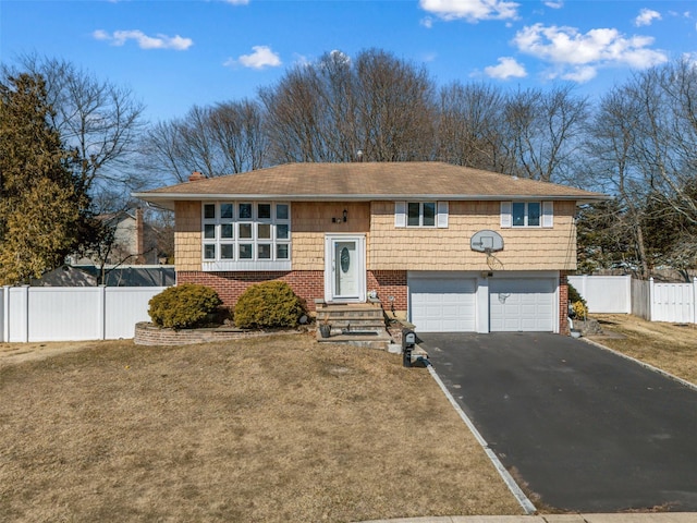 split foyer home with brick siding, an attached garage, a front yard, fence, and driveway