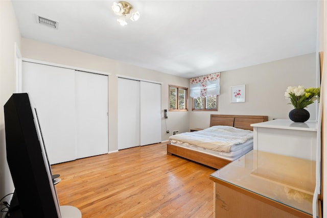 bedroom with multiple closets, visible vents, and light wood-style flooring