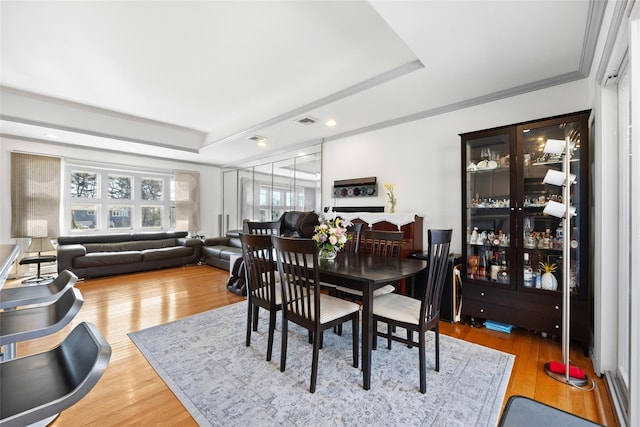 dining area featuring visible vents, a tray ceiling, wood finished floors, and ornamental molding