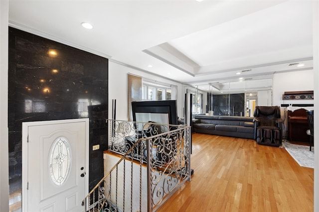 entryway featuring light wood finished floors, ornamental molding, a raised ceiling, and recessed lighting