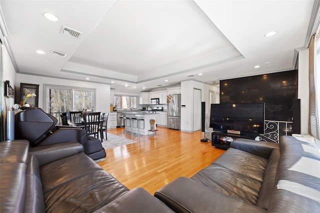 living area featuring light wood-style flooring, a raised ceiling, visible vents, and recessed lighting