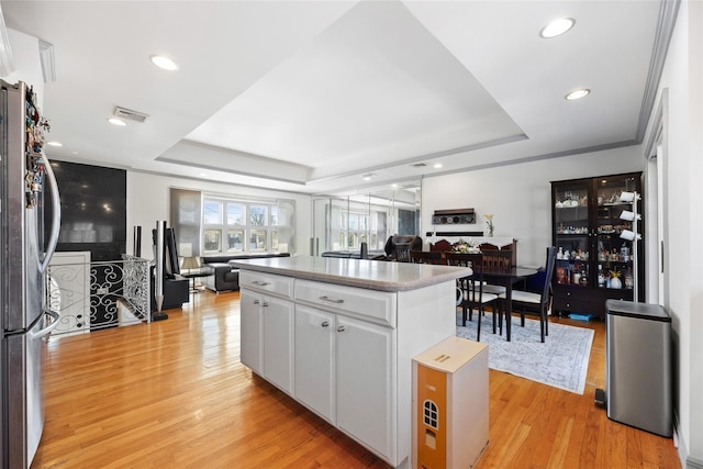 kitchen with a kitchen island, a raised ceiling, freestanding refrigerator, and light wood-style floors