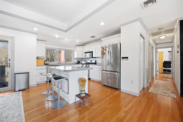 kitchen with visible vents, light wood-style flooring, appliances with stainless steel finishes, a breakfast bar area, and white cabinetry