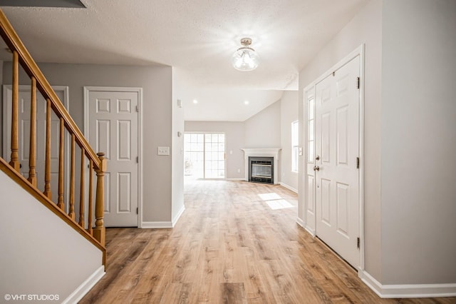 foyer entrance with baseboards, a fireplace with flush hearth, stairway, a textured ceiling, and light wood-style floors