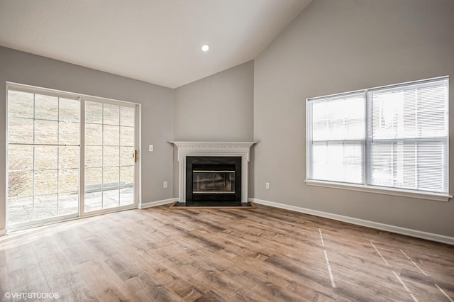 unfurnished living room with a fireplace with flush hearth, lofted ceiling, baseboards, and wood finished floors