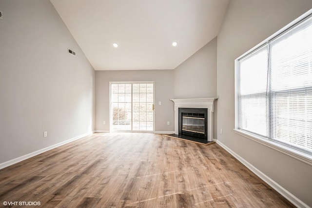 unfurnished living room featuring baseboards, visible vents, wood finished floors, and a glass covered fireplace