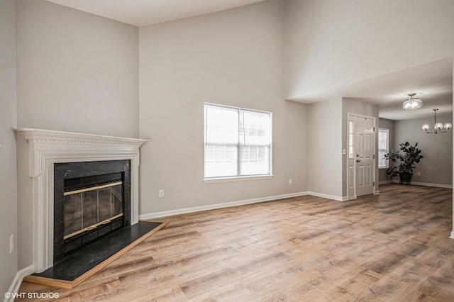 unfurnished living room with a notable chandelier, wood finished floors, a glass covered fireplace, and baseboards