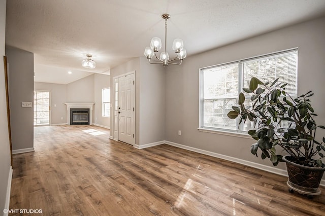 interior space with a textured ceiling, wood finished floors, baseboards, a glass covered fireplace, and an inviting chandelier