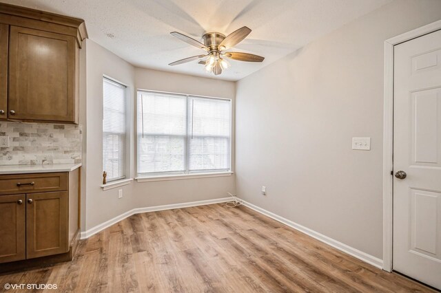 unfurnished dining area featuring ceiling fan, light wood finished floors, and baseboards