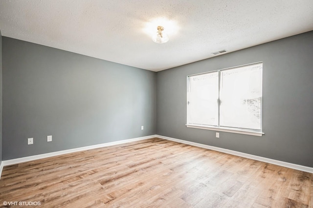 spare room with a textured ceiling, wood finished floors, visible vents, and baseboards