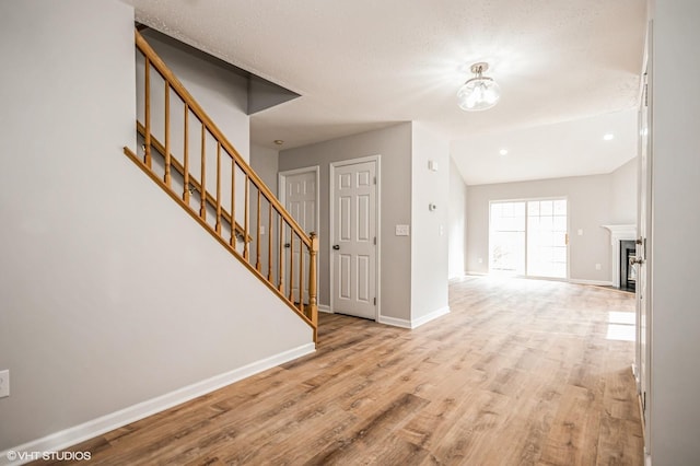 interior space featuring stairs, a fireplace, light wood-style flooring, and baseboards