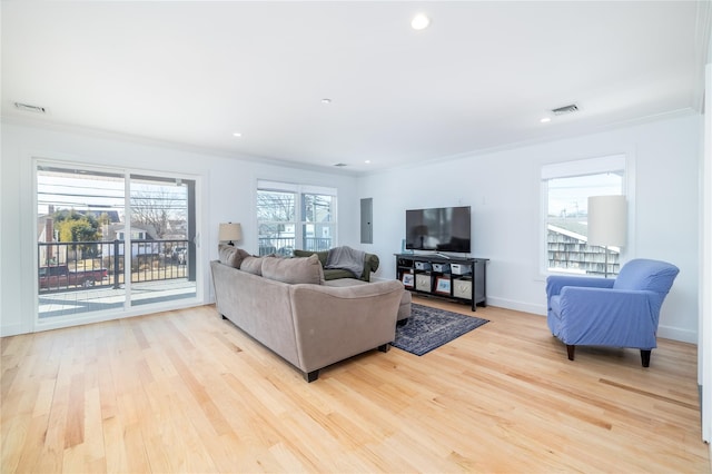 living area with ornamental molding, light wood-type flooring, electric panel, and visible vents