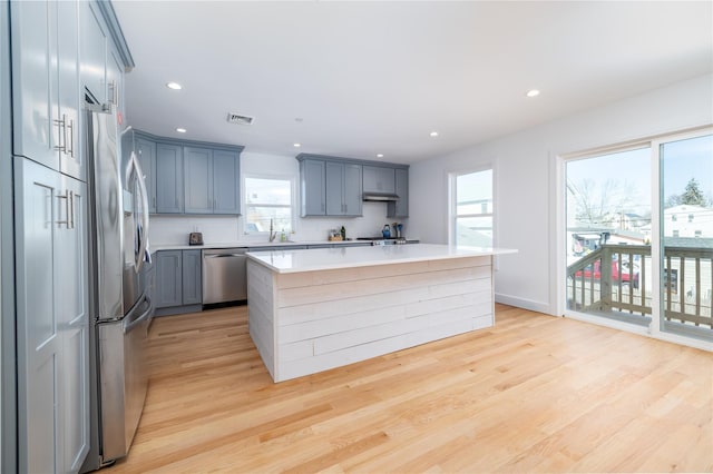 kitchen with light wood finished floors, stainless steel appliances, light countertops, visible vents, and under cabinet range hood