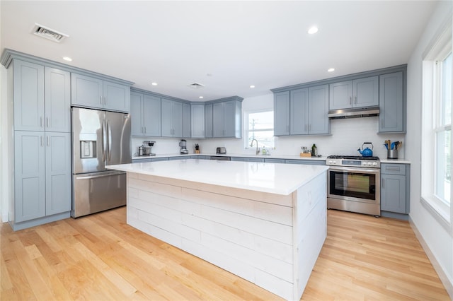 kitchen featuring under cabinet range hood, a kitchen island, a sink, visible vents, and appliances with stainless steel finishes