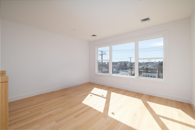 unfurnished room featuring baseboards, visible vents, and wood finished floors