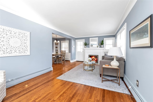 living area with baseboard heating, an inviting chandelier, a glass covered fireplace, and wood finished floors