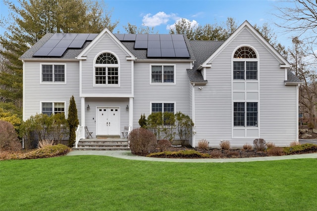 view of front of house with a shingled roof, a front yard, and roof mounted solar panels